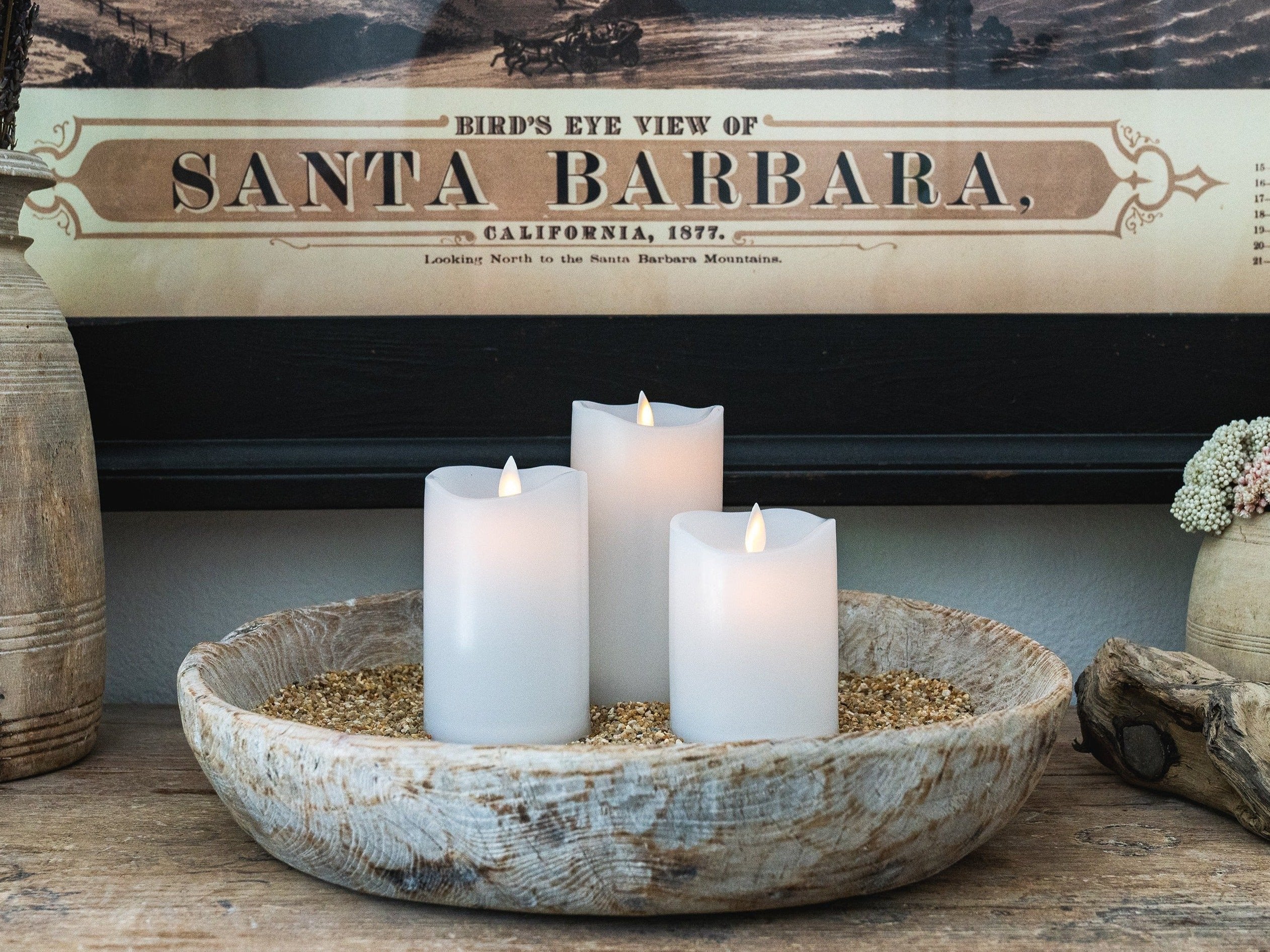 Antique wooden dough bowl with a set of 3 white flameless candles on a antique wooden buffet