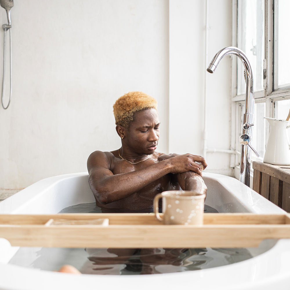 Man washing himself in the bath with a citrus soap bar made by Mumu Bath products