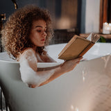 woman in a bath tub reading and relaxing by using an Organic French Clay Facial Soap